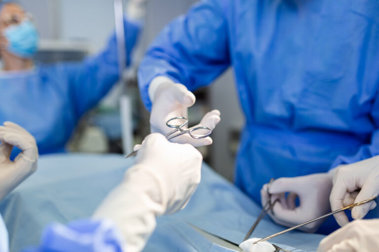 doctor and nurse medical team are performing surgical operation at emergency room in hospital. assistant hands out scissor and instruments to surgeons during operation